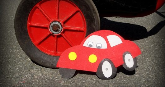 rotes Auto aus Tonkarton gebastelt steht neben einem roten Reifen aus Asphalt