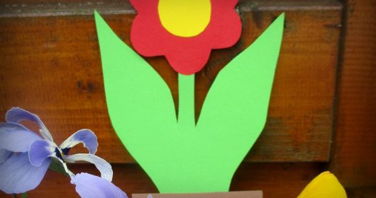 Rot-Grüne Blume aus Tonkarton vor einem Holzbalken