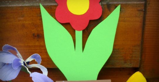 Rot-Grüne Blume aus Tonkarton vor einem Holzbalken