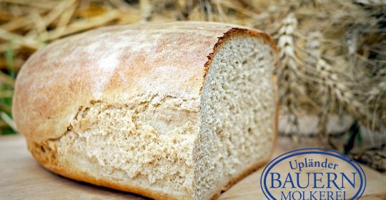 Ein halbes Brot auf einem Holzbrett vor Weizen