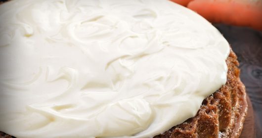 Möhrenkuchen mit weißer Glasur, Karotten im Huntergrund