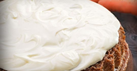 Möhrenkuchen mit weißer Glasur, Karotten im Huntergrund