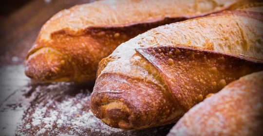 Nahaufnahme von drei Baguettes auf einem dunklen Holzbrett mit Mehl bestreut