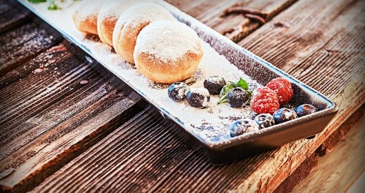 längliche Porzellanschale mit Berlinern mit Puderzucker und Früchten bestreut