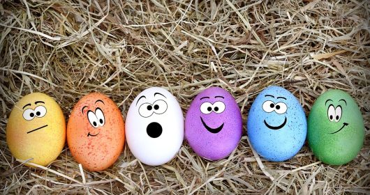 Bunte Eier mit aufgemalten Gesichtern aufgereiht auf Stro