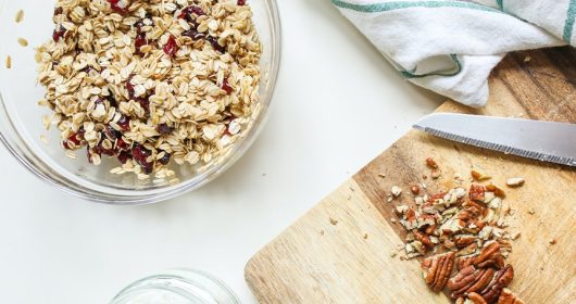 Glasschüssel mit Müsli neben einem Holzbrett mit gehackten Walnüssen