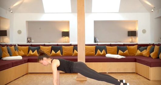 Frau macht Sportübungen auf einer rosa Matte vor einem Sofa