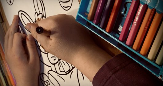 Kind malt ein Ausmalbild vom Osterhasen aus, bunte Stifte liegen auf dem Tisch