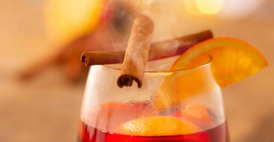 Ein Glas Glphwein mit Zimtstangen und Orangen auf einem Holztisch