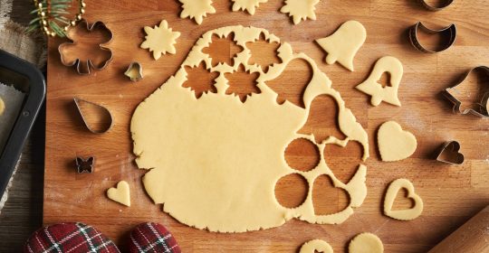 ausgerollter Teig für gesundes Weihnachtsgebäck mit zuckerfreien, ausgestochenen Keksen in Stern und Glockenform