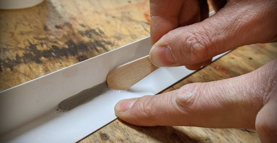 Nahaufnahme eines Holzspatels, der eine Silikonfuge glatt zieht