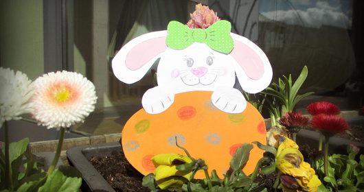Weißer Hase und Orangenes Osterei aus Tonkarton in einem Blumenbeet