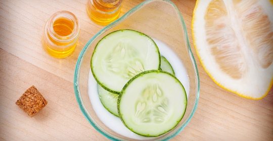 Glas mit Gurken neben Zitronenscheiben und kleinen Gläsern voller Honig