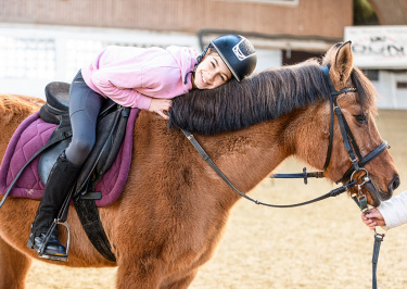 Kinder sitzt auf einem Pferd und schmiegt sich mit ihrem Kopf an das Pferd