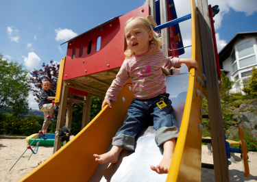 Kleinkind rutscht die Rutsche auf dem Spielplatz runter
