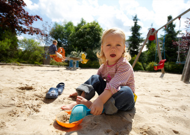 Kleinkind sitzt im Sandkasten auf dem Spielplatz